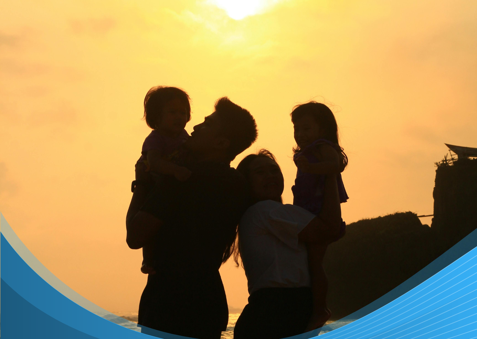 Silhouetted family with parents holding their two young children against a golden sunset at the beach.
